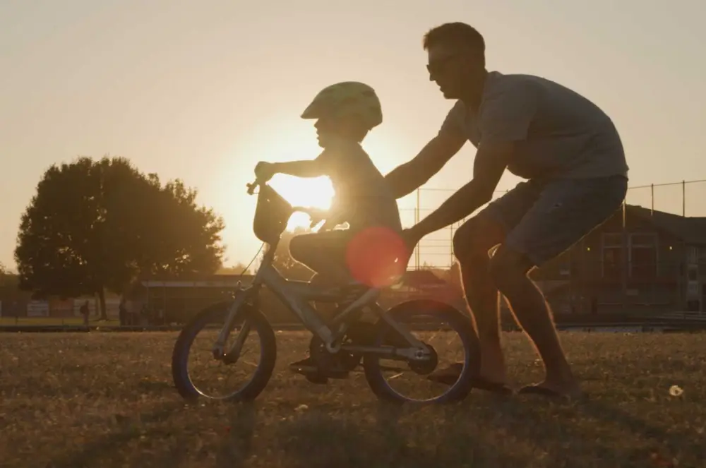 Father helping child ride a bicycle at sunset