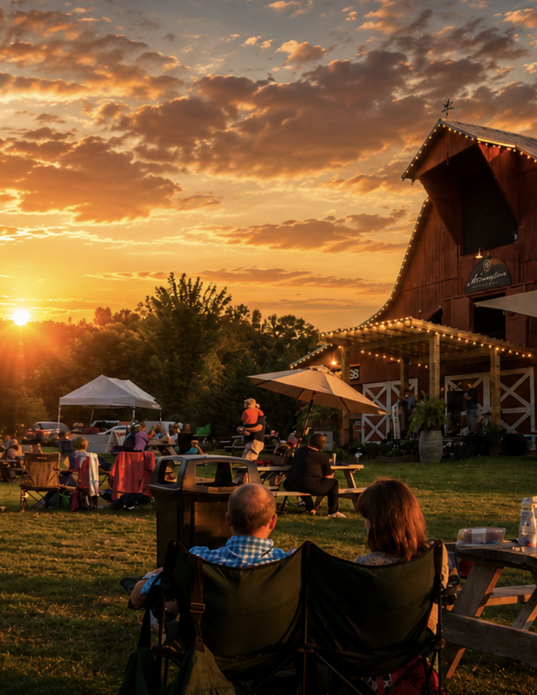Guests gathered at sunset outside a rustic barn venue with string lights and picnic tables